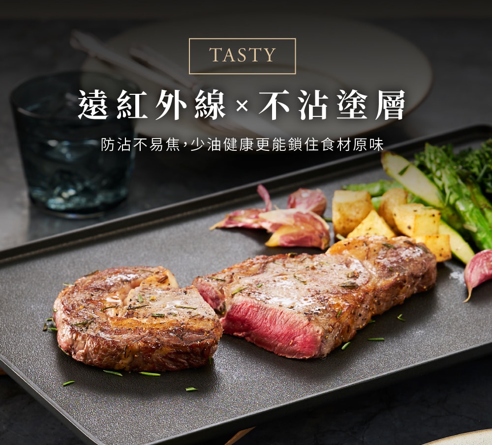 平坦的黑色電烤盤上，烤著兩塊多汁的牛排，旁邊配有烤馬鈴薯塊和綠蘆筍，還有大蒜和迷迭香裝飾。