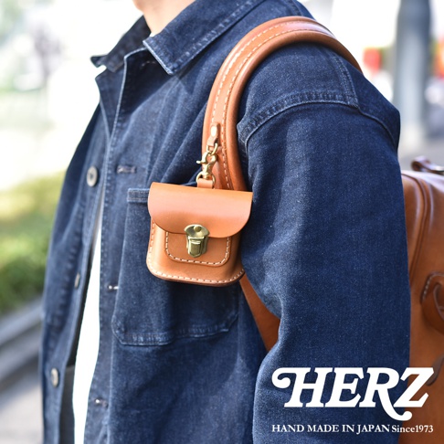 職人手作皮革耳機收納包，淺棕色，方形小巧設計，附有金屬鎖扣和掛鉤，可掛於背包肩帶上。