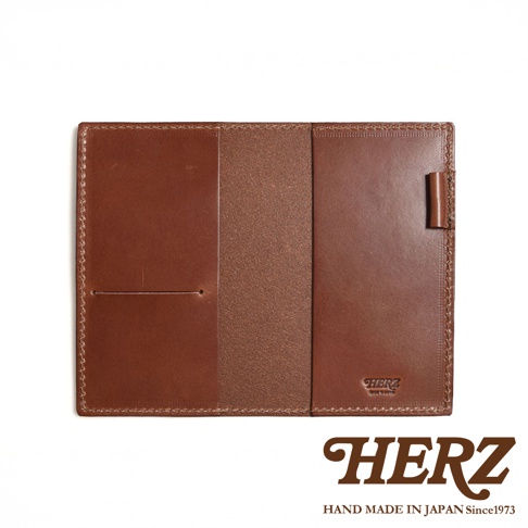 職人手作皮革輕便記事本書套，採用鞣製皮革製成，顏色為經典棕色。書套設計簡潔，內部有兩個主要隔層，左側隔層設有票卡夾層。右側隔層外側有一個皮革筆套，方便攜帶筆。整體縫線工整，展現職人細膩的工藝。