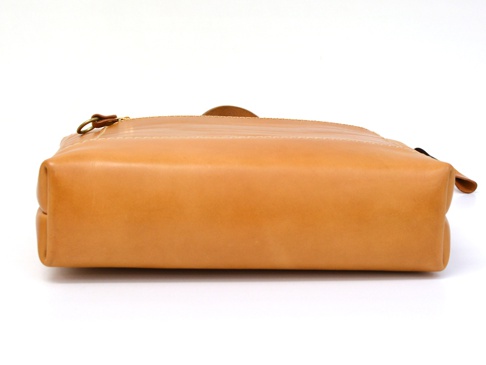 職人手作皮革威靈頓直式拉鍊托特包 (T-151)，採用天然皮革材質，呈現溫潤的焦糖棕色。包款側面可見拉鍊和金屬拉環，以及細緻的縫線，整體造型簡潔俐落。