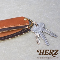 職人手作皮革Organ拉鍊鑰匙包，呈現自然棕色，搭配黃銅色五金配件，拉鍊為黑色，車縫線為米色，鑰匙包內含數支銀色金屬鑰匙，整體以簡約設計展現皮革質感。