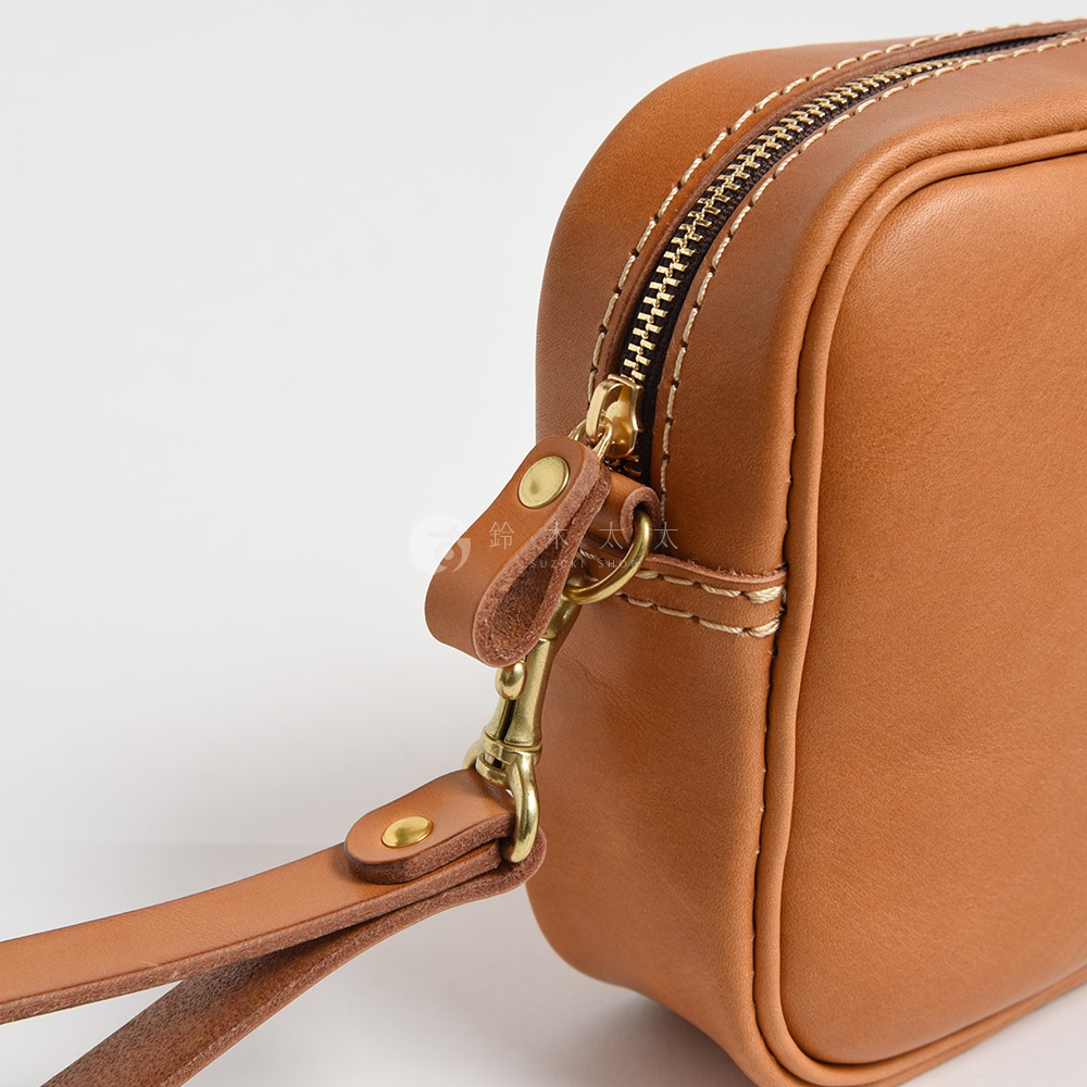 職人手作皮革萬用手提包，採用棕褐色皮革，配有金色拉鍊和可拆式扣環，展現精緻的縫線細節。