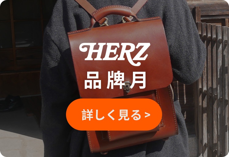 一名身穿灰色毛衣的人背著一個棕色皮質後背包，包上印有白色字樣「HERZ 品牌月」，下方有一個橘色的按鈕，上面寫著「詳し見**」。