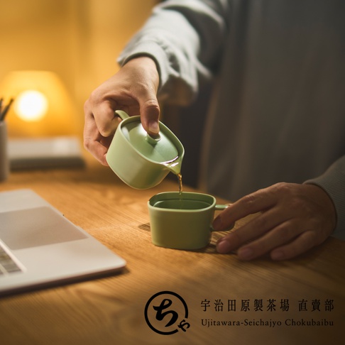 在溫暖的燈光下，有人正使用宇治田原製茶場的淺綠色美濃燒一人用茶壺將茶水倒入同款茶杯，桌面上擺放著筆記型電腦，展現出靜謐且優雅的辦公室品茶時光。