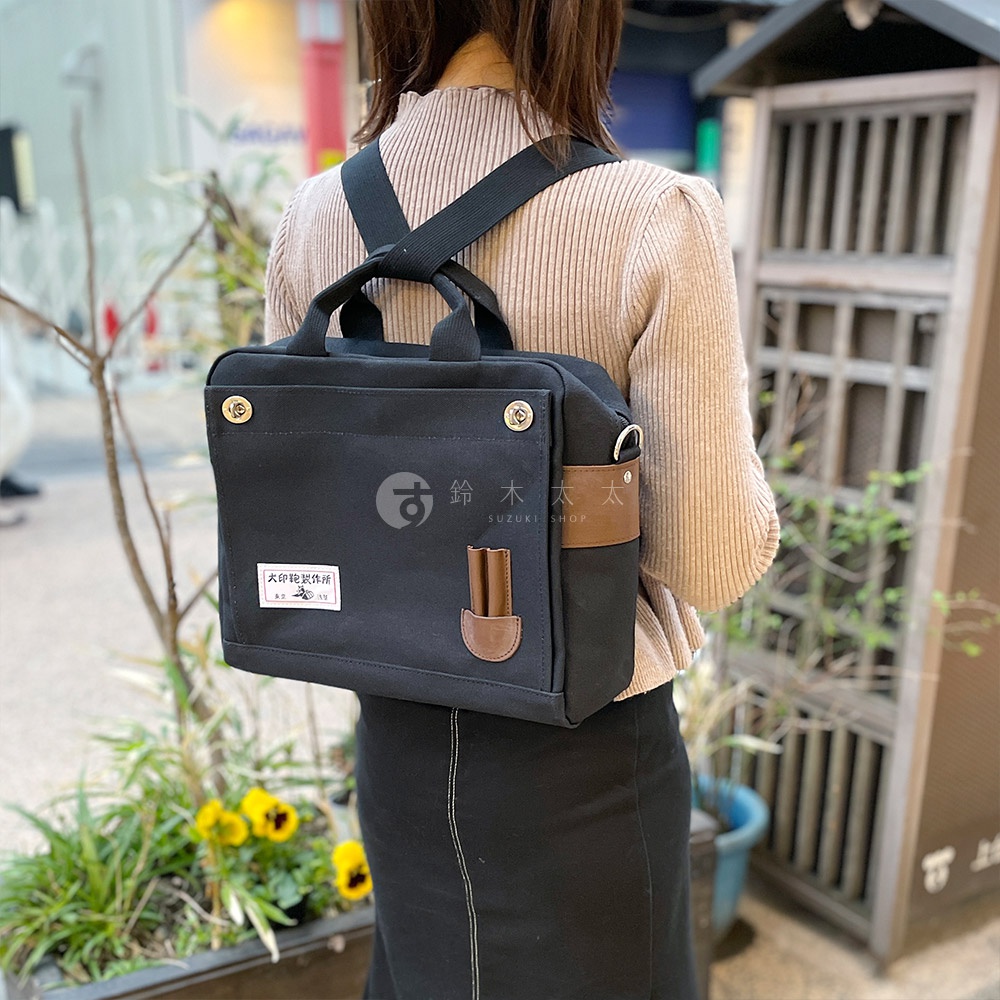黑色純棉帆布三用橫式側背包，配有棕色皮革裝飾和可調節背帶，展現簡約時尚風格。