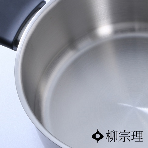 柳宗理不鏽鋼霧面雙耳鍋俯視特寫，可見鍋具內部金屬拉絲紋理與光滑的底部質感，左側裝有黑色鍋耳，右下角印有柳宗理品牌標誌。