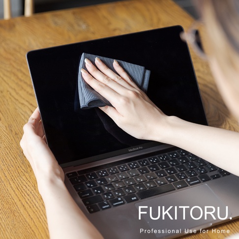 一隻手拿著灰色條紋超細纖維清潔布擦拭筆記型電腦螢幕。