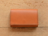 淺棕色皮革證件夾，有手工縫線裝飾，風格簡約，置於木紋桌面。