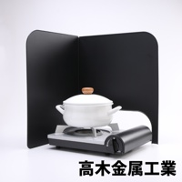 黑色 L 型折疊擋油板，兩塊面板以直角連接，中間放置一個帶木質鍋蓋把手的白色鍋具，鍋具置於灰色與黑色相間的爐具上。
