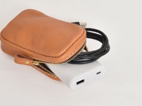 職人手作皮革菸盒收納包 (KF-111)，採用淺棕色牛皮製作，側邊有縫線與金色拉鍊，包款部分開口露出一個白色行動電源及一條黑色充電線。