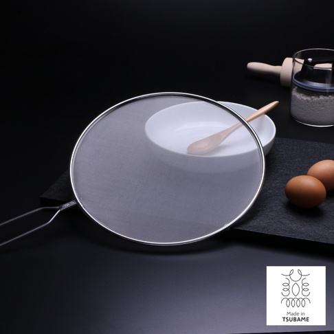 銀色金屬邊框的圓形透視防噴濾網，網面細密，帶有金屬把手。背景有白色碗、木勺、兩個雞蛋和一個裝有麵粉的透明玻璃罐，以及一個木質擀麵棍。