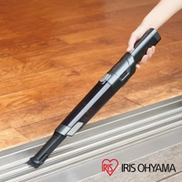 一支黑色和銀色的攜帶式充電吸塵器，配有刷頭，正在被手握著清潔木地板的縫隙。