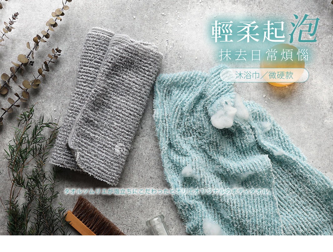兩條質地粗糙的毛巾，一條是灰色，一條是藍色，上面有泡泡，旁邊還有綠色的植物和木刷