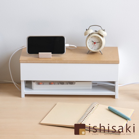 白色木質附蓋電線收納盒，頂部為淺木紋桌面，放置著充電中的手機及一個米白色復古鬧鐘。收納盒下方層架內有白色延長線，插座處有橘色指示燈亮起。