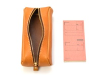 職人手作皮革圓角收納筆袋，淺棕色皮革材質，拉鍊半開，露出內部深棕色皮革。旁邊有一個粉紅色小筆記本，印有英文 Reserve 和數字 No. 00。