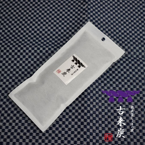 白色無紡布包裝的細長型木炭，上面印有「古來炭」的黑色日文標誌，放置於深藍色格紋背景上。