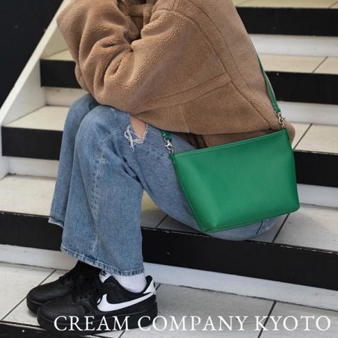 綠色皮革手提包，帶有銀色鏈條和皮革肩帶，斜挎於穿著淺棕色毛絨外套和牛仔褲的模特身上。