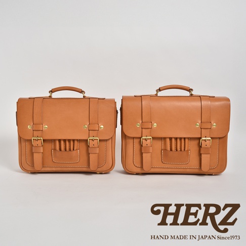 兩個棕褐色皮革製成的傳統歐風三用學生包，一前一後並排展示，皆有翻蓋、金屬釦環、提把及雙肩帶。