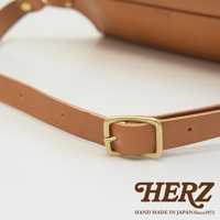 職人手作皮革立體斜背包 F-2，特寫展示帶有黃銅扣環的棕色皮革肩帶，簡約設計，展現皮革質感。