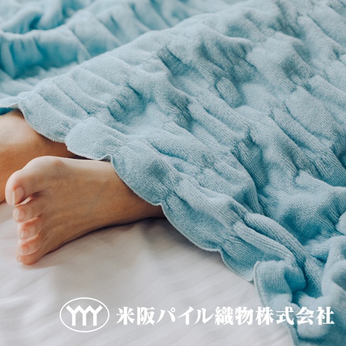 淺藍色輕暖柔蓬抗摩四季毯，織紋立體，質地柔軟，覆蓋著人腿部，毯邊有波浪狀荷葉邊設計。