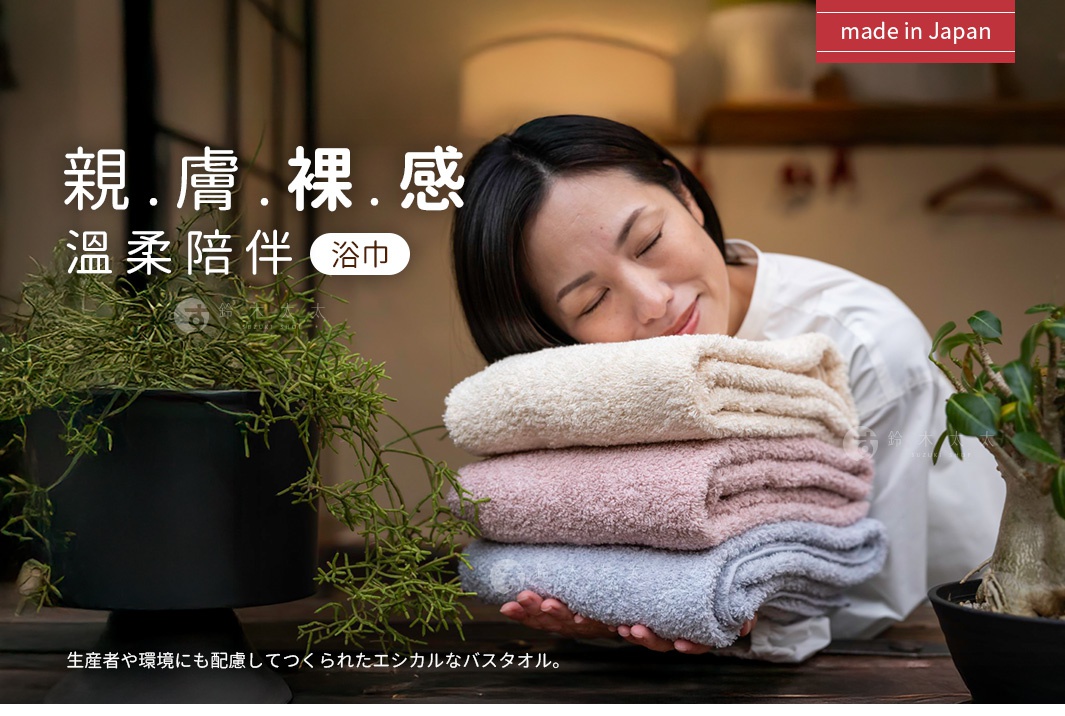 疊放的有機棉浴巾，顏色為米白色、淡粉色與淺灰色，質感蓬鬆柔軟。