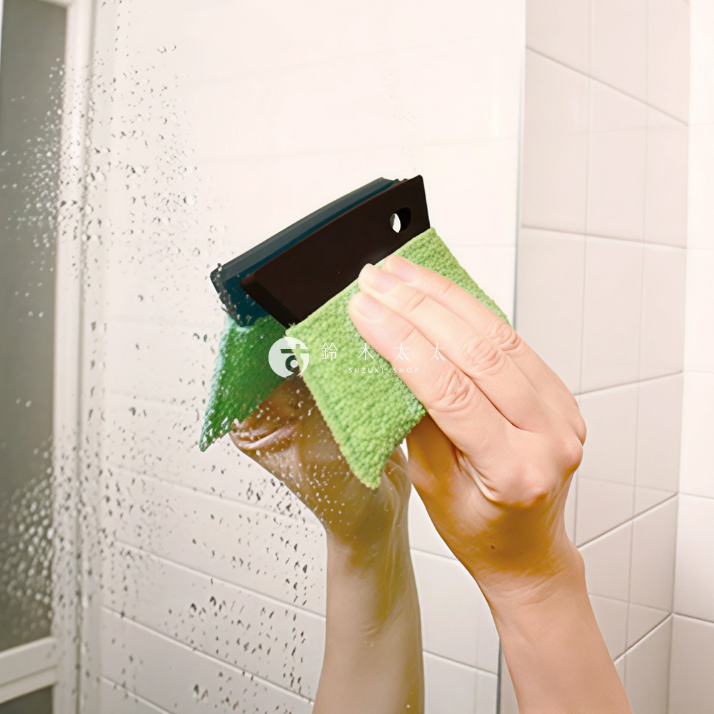 手拿綠色清潔布和刮刀，正在清潔佈滿水珠的鏡子