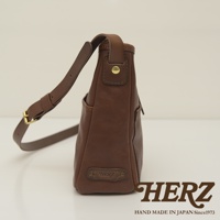 職人手作皮革輕便單肩側背包，採用棕色鞣革，設有可調節肩帶及金屬釦，底部有品牌標誌壓印。