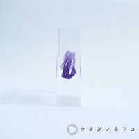 透明壓克力方塊中封存著一塊紫色紫水晶晶體，晶體呈現不規則的切面，部分區域透光。