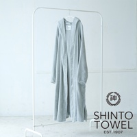 一件淺灰色連帽浴袍，採用蓬鬆有機棉材質，垂掛在白色衣架上，浴袍有兩個對稱的口袋，右側有品牌標誌。