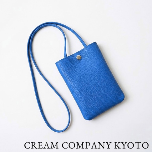 由日本京都製造的 CREAM COMPANY KYOTO 職人手作隨身手機包，採用鮮豔亮眼的藍色紋理牛皮材質製成，配備細長肩背帶及簡約金屬扣開口設計，整體造型輕巧簡約，適合日常隨身收納手機等隨身小物。