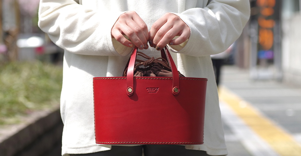 紅色皮革束口手提包，附有兩條皮革提把，包身縫線清晰，中央壓印品牌標誌。