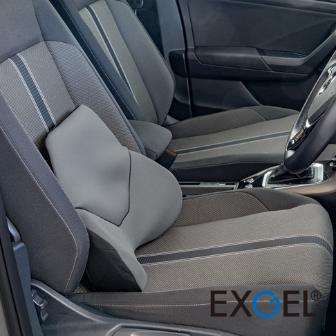 汽車駕駛座上放置著一個灰色日本EXGEL品牌的一體式透氣背靠墊，該靠墊設計符合人體工學，能有效支撐腰部，並與深色系的車內座椅及周邊內飾自然融合，呈現舒適且實用的駕駛空間配置。