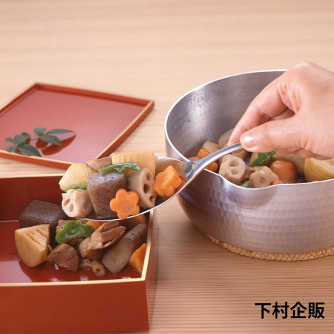 不鏽鋼分食匙盛著多種燉煮食材，包含蓮藕、紅蘿蔔、香菇、竹筍、芋頭等，食材呈現天然色澤，部分紅蘿蔔切成花形。分食匙傾斜，食材部分落入一旁紅漆木盒中。