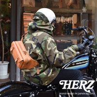 一件棕褐色皮革斜背包，斜背在身穿迷彩外套的人身上，該人正騎乘於哈雷機車上。