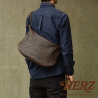 職人手作皮革Organ單肩半月包，深棕色，採用紋理皮革製成，斜背於身穿深藍色襯衫的男子身上。