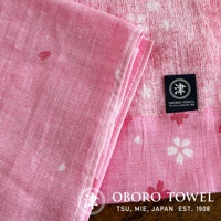 粉紅色紗布毛巾，帶有日式花朵圖案和 OBORO TSU, MIE, JAPAN EST. 1908 的品牌標籤