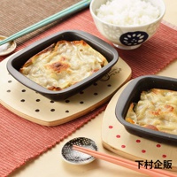 兩個黑色的迷你方形烤盤，裝有烘烤過的點心，放在木質隔熱墊上，墊上有圓點圖案。旁邊有一碗白飯、一雙筷子及一個小碟。