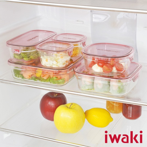 多個透明耐熱玻璃保鮮盒，配有粉紅色密封蓋，部分盒內裝有蔬菜沙拉、鮭魚、玉米粒、番茄乳酪及壽司捲。冰箱架上擺放著紅色蘋果、黃色蘋果和檸檬。