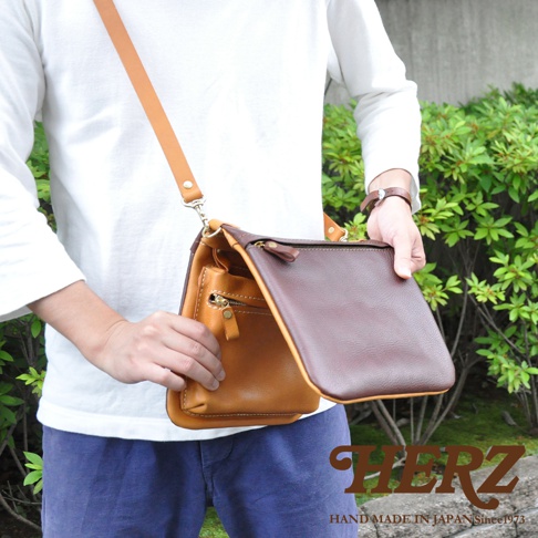職人手作皮革翻轉雙色直式斜背包，採用兩種不同色調的皮革拼接，包含焦糖棕色和深棕色，配有可調節的皮革斜背帶及拉鍊。