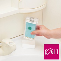 透明壓克力盒裝著藍色洗衣皂，盒內有彈簧，一隻手正將其從一個白色小盒上方移開。