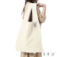 一名女子手持一個米白色的大容量摺疊環保隨行袋，袋子材質光滑，有兩個寬肩帶，袋子側面有一個灰色小標籤。