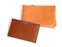 雙層皮革收納組，包含一個淺棕色卡夾，夾內有一張藍色幾何圖案卡片，以及一個較大的橘棕色拉鍊零錢包，兩者皆有白色縫線裝飾，材質皆為皮革。
