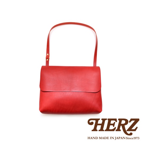 紅色皮革經典郵差包，翻蓋設計，附有可調整長度的肩帶，整體為簡約風格。