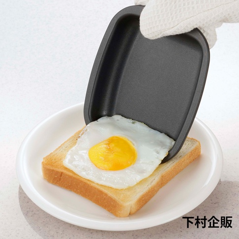 一個黑色迷你方形烤盤，正覆蓋在一片吐司上的煎蛋。烤盤帶有防燙手套，放在白色盤子上。