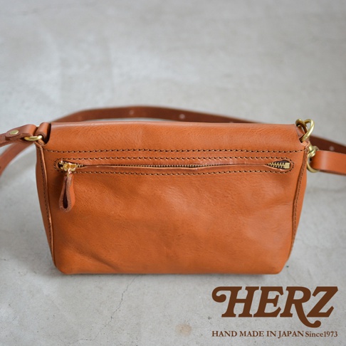 一個棕褐色的皮革斜背包，正面有一個拉鍊口袋，並附有皮革背帶。