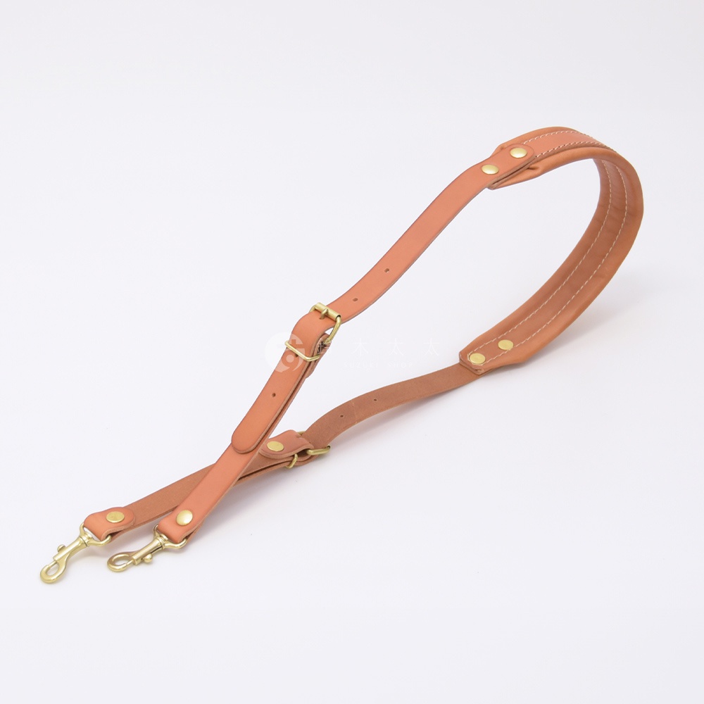 職人手作皮革加厚減壓肩背帶，呈現自然的淺棕色皮革質感，配有黃銅色金屬扣環和鉚釘，設計簡約實用。