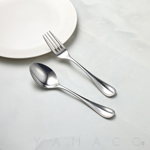 不鏽鋼叉匙兩件組，叉子和湯匙皆有珠狀邊緣設計，擺放在白色餐盤旁。