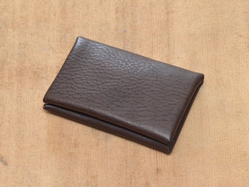 深棕色皮革製成的雙開式卡片收納夾，表面紋理清晰，放置於淺棕色木質背景上。