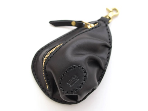 職人手作黑色皮革餃子造型零錢包，帶有金色拉鍊和鉤扣，邊緣縫線明顯，正面有一個壓有品牌標誌的圓形皮革貼片。