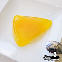 黃色果凍呈三角形，質地光滑，放在白色盤子上，旁邊有一支銀色湯匙。